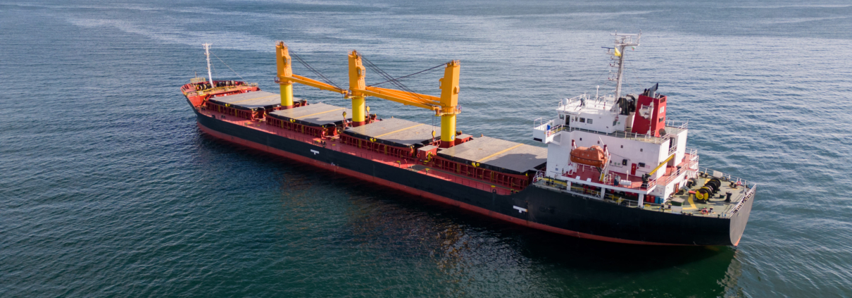 Buque de carga navegando en mar abierto, con casco azul y franja roja, impulsado por motor diésel marino
