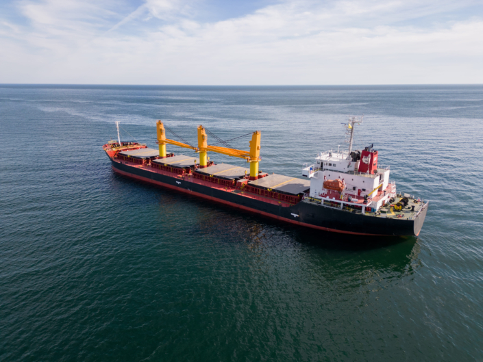 Buque de carga navegando en mar abierto, con casco azul y franja roja, impulsado por motor diésel marino